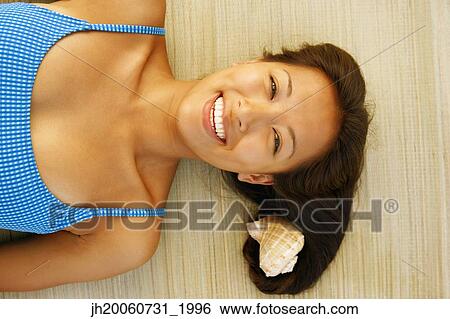Stock Photograph - Asian woman laying next to seashell. Fotosearch