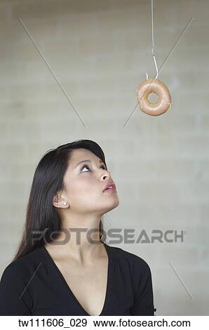 Asian woman looking at doughnut on hook View Large Photo Image Stock Photo - Asian woman looking at doughnut on hook. Fotosearch