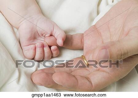 Stock Image - Close up of baby holding father’s finger. Fotosearch