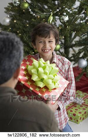 Stock Image - Hispanic boy giving Christmas gift to father. Fotosearch