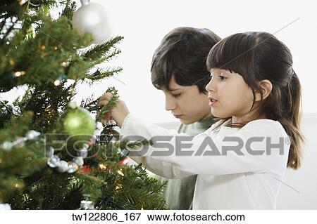 Stock Photo - Hispanic brother and sister decorating Christmas tree. Fotosearch