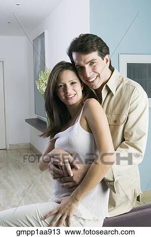 Stock Image - Hispanic couple hugging indoors. Fotosearch