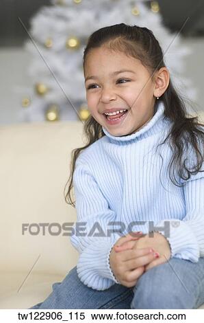 Stock Photography - Hispanic girl laughing in front of Christmas tree. Fotosearch