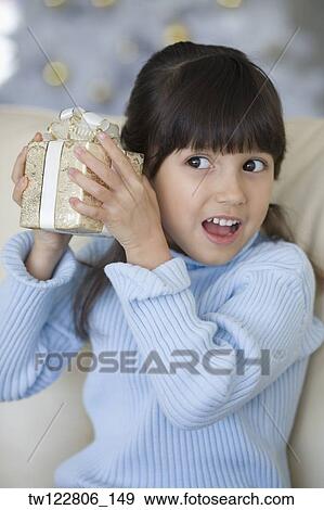 Hispanic girl shaking Christmas gift View Large Photo Image Stock Photo - Hispanic girl shaking Christmas gift. Fotosearch
