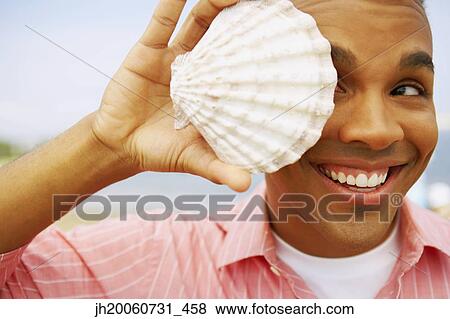 Hispanic man holding seashell over eye View Large Photo Image Stock Photo - Hispanic man holding seashell over eye. Fotosearch