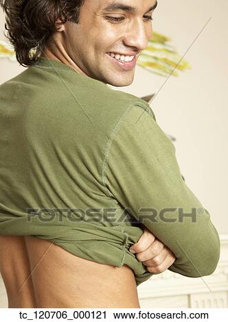 Stock Image - Hispanic man removing shirt. Fotosearch