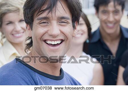 Hispanic man smiling with friends in background View Large Photo Image Stock Photo - Hispanic man smiling with friends in background. Fotosearch
