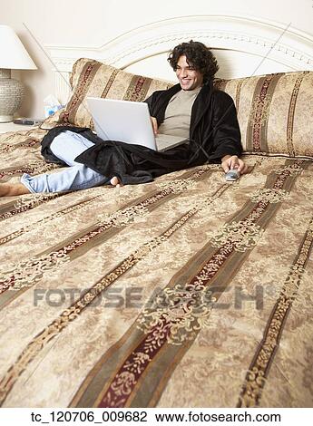 Hispanic man typing on laptop in bed View Large Photo Image Stock Image - Hispanic man typing on laptop in bed. Fotosearch
