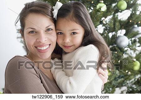 Hispanic mother and daughter hugging next to Christmas tree View Large Photo Image Stock Photo - Hispanic mother and daughter hugging next to Christmas tree. Fotosearch