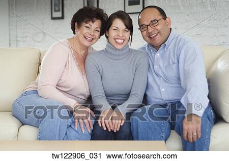 Stock Image - Hispanic parents and adult daughter on sofa. Fotosearch