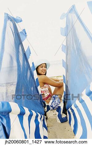 Stock Photo - Hispanic woman sitting next to beach sun shade. Fotosearch