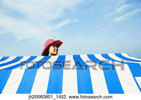 Stock Image - Hispanic woman standing behind beach sun shade. Fotosearch