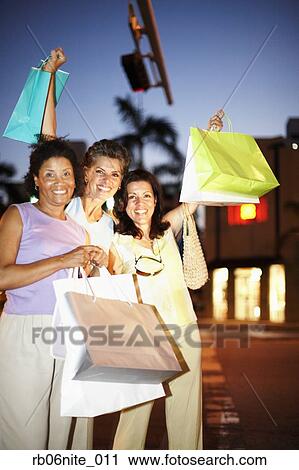 Stock Image - Hispanic women smiling with shopping bags at night. Fotosearch