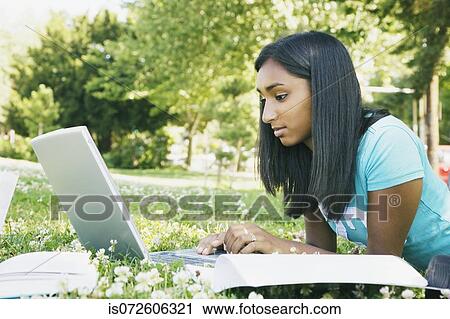 Stock Image - Indian female college student working on laptop in grass. Fotosearch