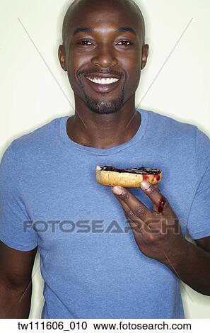 Stock Image - Portrait of African man eating bagel. Fotosearch