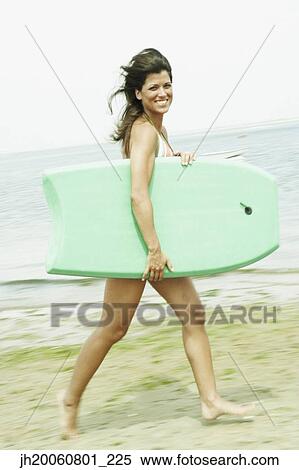 Stock Photography - Woman carrying boogie board at beach. Fotosearch