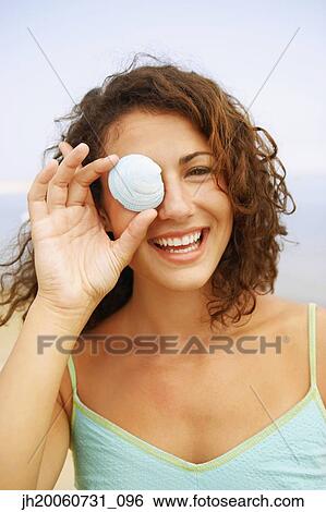 Stock Photograph - Woman holding seashell over eye. Fotosearch