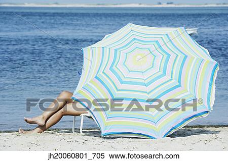 Stock Photography - Woman sitting under beach umbrella. Fotosearch