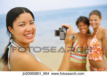 Woman video recording friends at beach View Large Photo Image Picture - Woman video recording friends at beach. Fotosearch