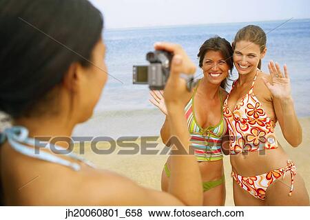 Stock Photo - Woman video recording friends at beach. Fotosearch