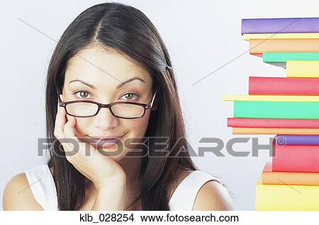 Picture - Woman wearing eyeglasses next to stack of books. Fotosearch