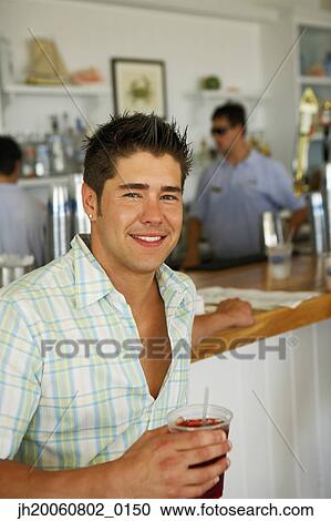 Stock Image - Young man drinking at bar. Fotosearch