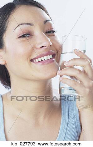 Young woman holding glass of water against face View Large Photo Image Stock Image - Young woman holding glass of water against face. Fotosearch