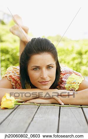 Stock Image - Young woman laying on deck. Fotosearch