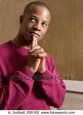 Stock Image - African man touching fingers to chin. Fotosearch
