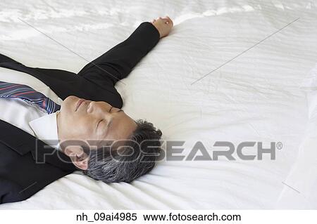 Stock Photography - Asian businessman laying on bed. Fotosearch