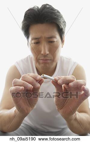 Stock Image - Asian man breaking cigarette in half. Fotosearch
