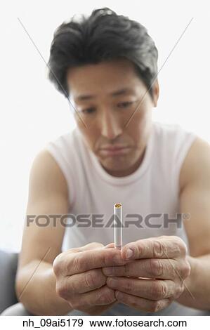 Asian man frowning at cigarette View Large Photo Image Stock Photo - Asian man frowning at cigarette. Fotosearch