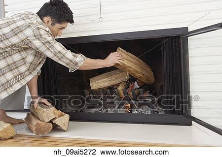 Stock Image - Asian man putting logs in fireplace. Fotosearch