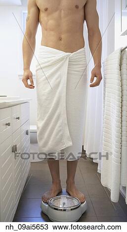 Stock Image - Asian man standing on bathroom scale. Fotosearch