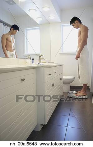 Stock Photo - Asian man standing on bathroom scale. Fotosearch