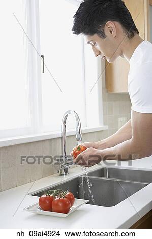 Asian man washing tomatoes in kitchen View Large Photo Image Picture - Asian man washing tomatoes in kitchen. Fotosearch