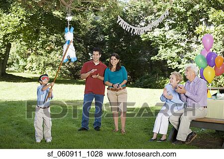 Family watching Hispanic boy hitting pinata at birthday party View Large Photo Image Stock Photo - Family watching Hispanic boy hitting pinata at birthday party. Fotosearch