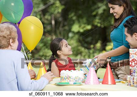 Stock Photo - Hispanic girl receiving gift at birthday party in park. Fotosearch