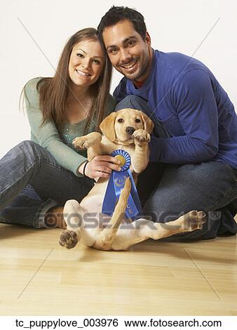Stock Photograph - Multi-ethnic couple holding puppy dog and blue ribbon. Fotosearch