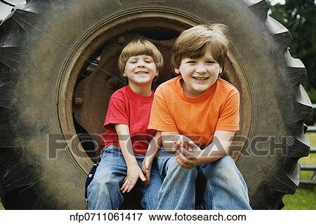 Two brothers sitting on tractor wheel View Large Photo Image Stock Photo - Two brothers sitting on tractor wheel. Fotosearch