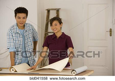 Stock Photo - Asian couple hanging wall paper. Fotosearch