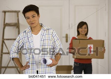 Stock Image - Asian couple with blueprints in new house. Fotosearch