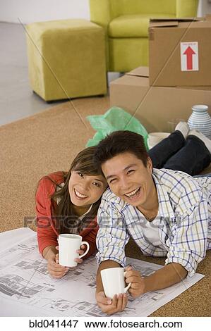 Stock Photo - Asian couple with blueprints in new house. Fotosearch