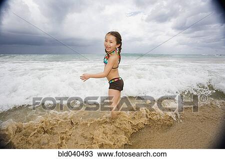 Stock Image - Asian girl playing in surf. Fotosearch
