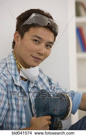 Picture - Asian man holding power sander. Fotosearch