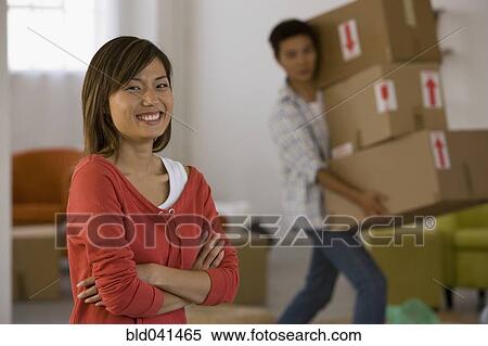 Stock Photography - Asian woman laughing while husband carries boxes. Fotosearch