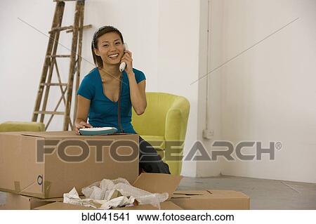 Stock Image - Asian woman talking on telephone in new house. Fotosearch