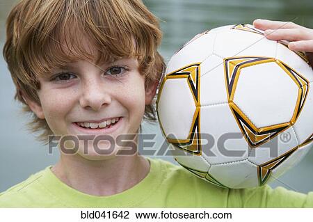 Stock Image - Boy holding soccer ball on shoulder. Fotosearch