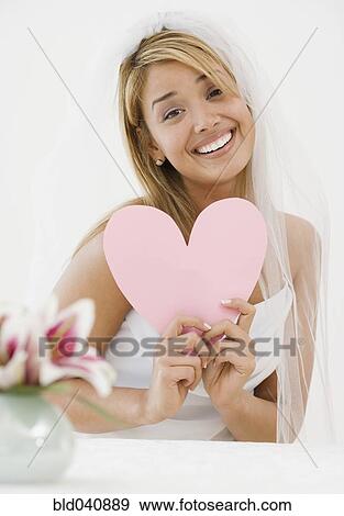 Stock Photo - Hispanic bride holding paper cutout heart. Fotosearch