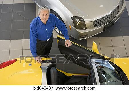 Stock Photo - Hispanic car salesman getting into new car. Fotosearch